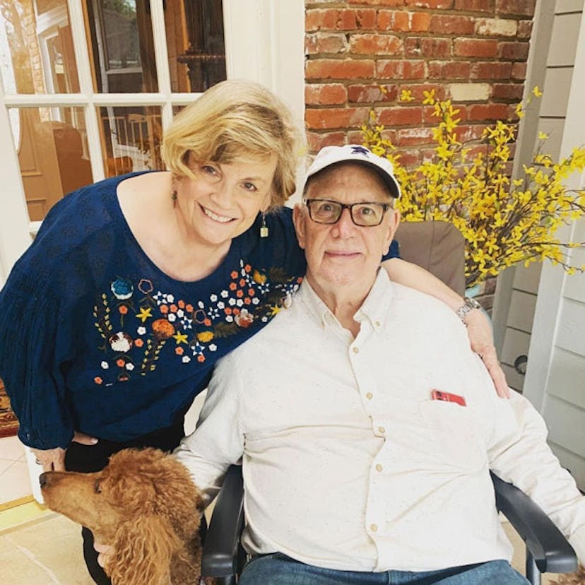 An elderly married couple smiling and posing at a terrace with their dog