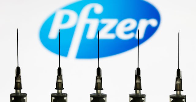 Medical syringes are seen with Pfizer company logo displayed on a screen in the background