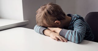 A young sad boy sitting alone in a classroom