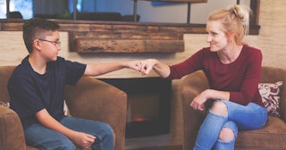 A Woman And A Boy Sitting On Armchairs Across From Each Other And Fist Bumping