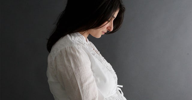 A worried pregnant woman with long dark hair looking at her belly