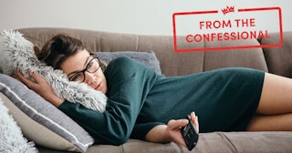Young woman lying down on a sofa, feeling depressed and changing channels on a TV remote.