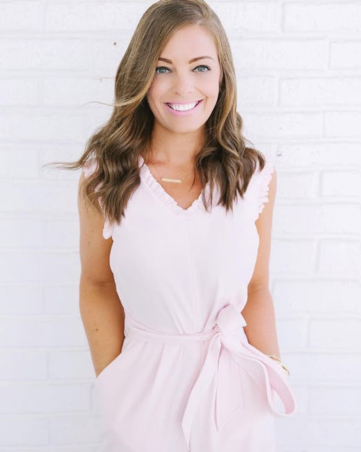 Stephanie Hanrahan in a pink dress smiling with a white brick wall in the background