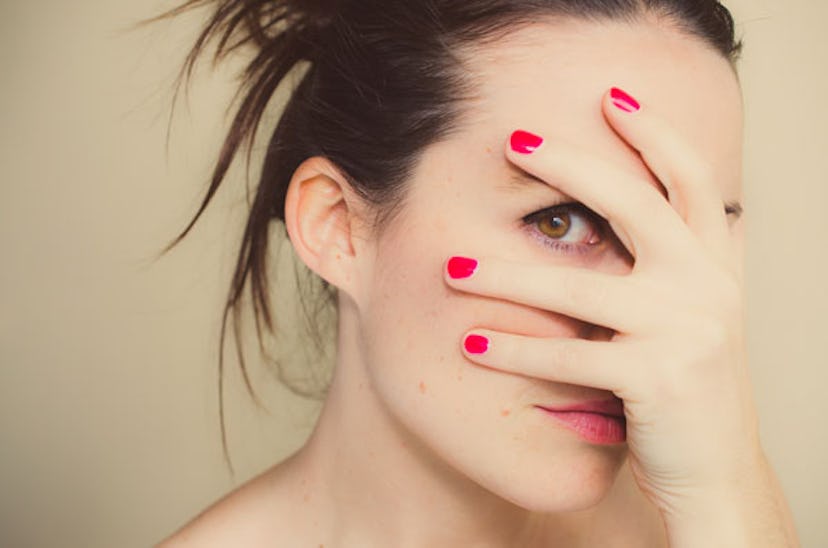 A red-nailed woman covering her face with her hand with one eye peeking through