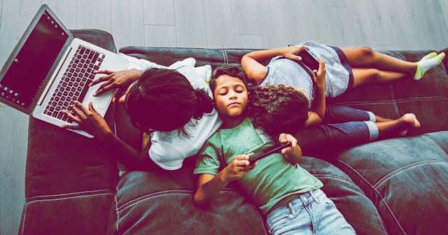 family sitting on the sofa at home and using digital devices. mother using laptop while her two chil...