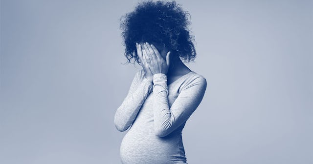  Pregnant woman covering her face while standing in front of a wall.