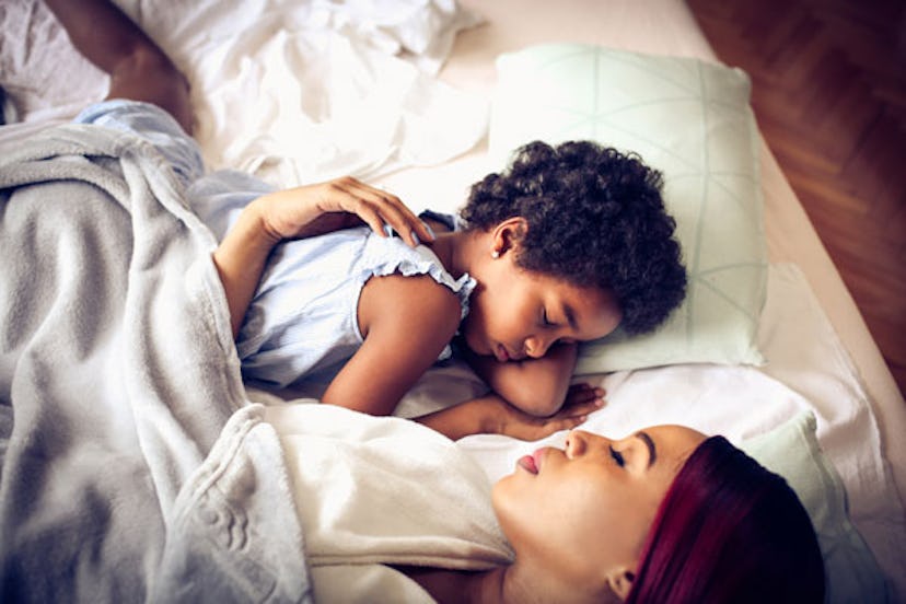 A mother and her child sleeping on a bed with heads turned toward each other