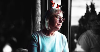 A woman in a blue sweater looking through a window with a sad facial expression