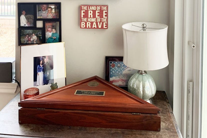A triangular wooden box next to a small white lamp and framed photographs on a small desk