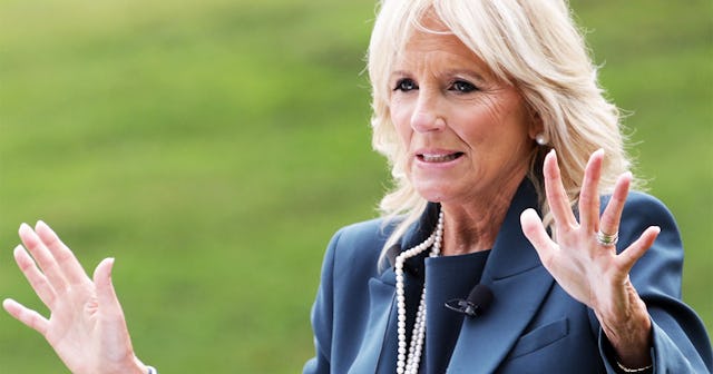 Jill Biden in a blue coat, pearl necklace and earrings with her arm raised
