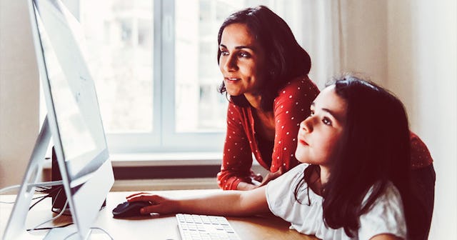A girl working on a computer while her mom is sitting next to her during homeschooling