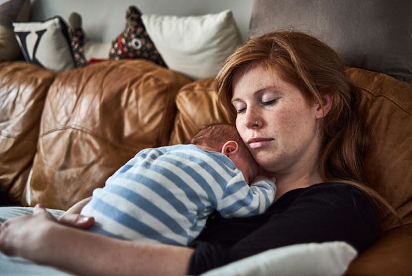 A single mom sleeping with her baby in the hands on a brown leather couch