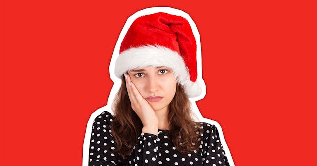 A woman with brown hair wearing a polka dot top and a Santa hat, her cheek resting on her hand, look...