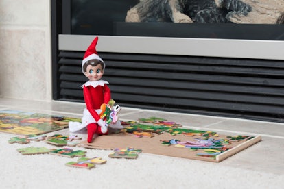 A wooden elf on the shelf toy, dressed in red with a red Santa hat