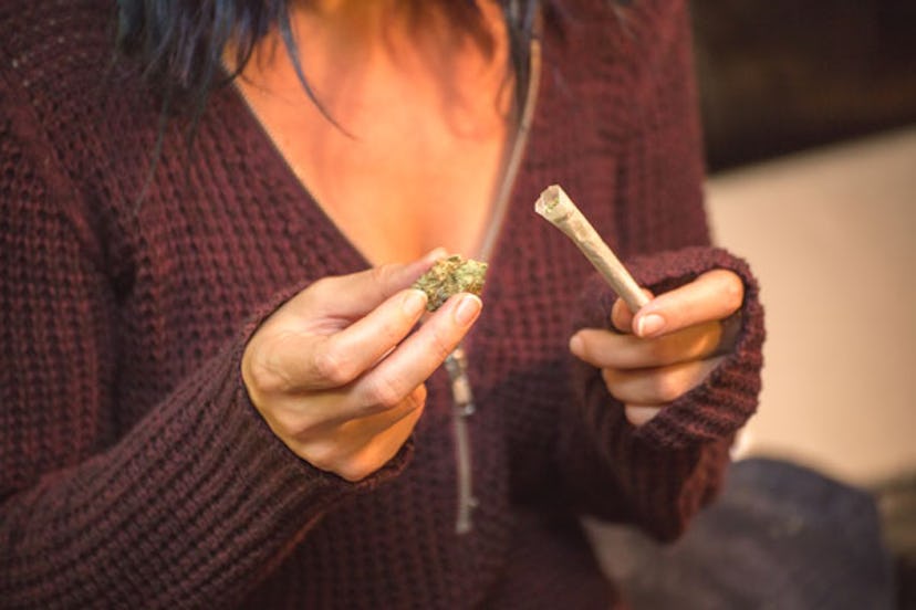 A woman putting a cannabis head into a rolled up smoking paper