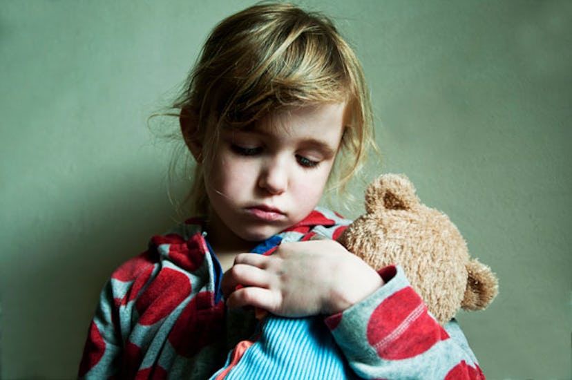 A sad little girl clutching a teddy bear