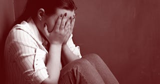 A victim of human trafficking sitting depressed in the corner of a room while covering her face with...