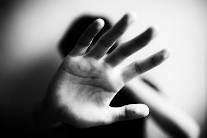 A close-up of the hands of a human trafficking victim covering their face in black and white