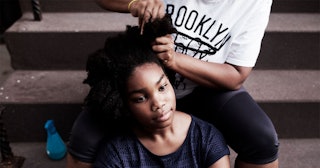 A mother of a child's black friend combing the hair of a teenage girl while sitting on steps
