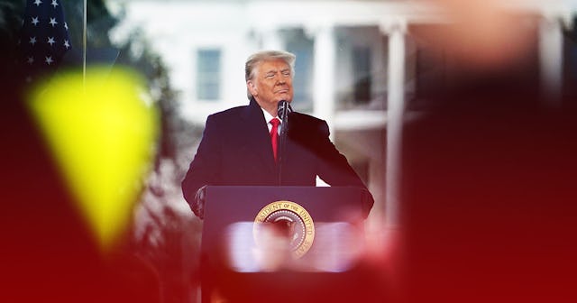 Politician Donald Trump wearing a black suit and red tie looking proudly at the audience on a stage ...