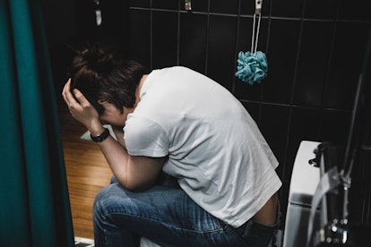 A woman sitting in the bathroom on a toilet and crying 