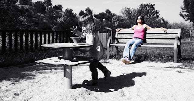 A woman is sitting on a bench at a playground while a girl is playing in front of her.