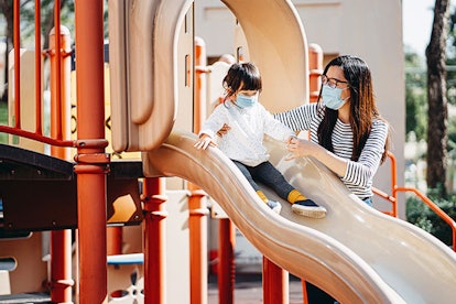 A woman holding her daughter on a slide, while both are wearing face masks