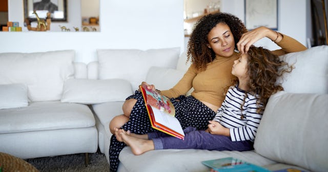 Mother and daughter sitting on a couch reading a book on a white couch in a living room