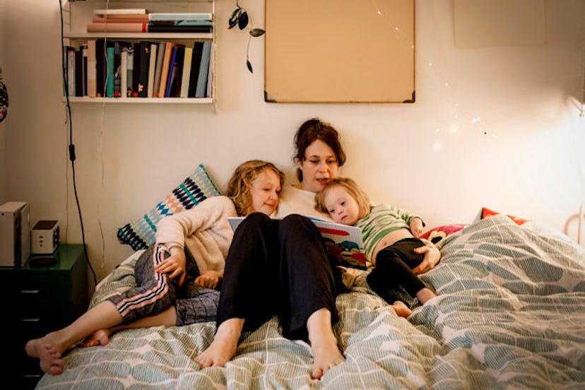 Mother with two daughters in bed reading a book while lying in a bed