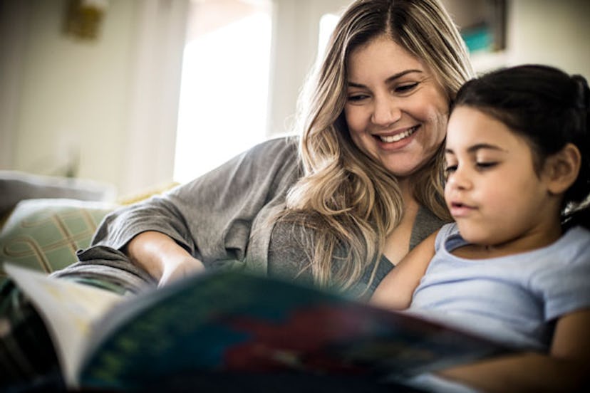 A smiling mother and daughter reading a book. 
