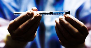 A medical worker in blue scrubs and white rubber gloves holding a COVID-19 vaccine injection 