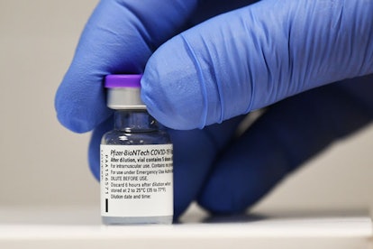A close-up of a medical worker's hand in blue rubber gloves holding the COVID-19 vaccine in a bottle