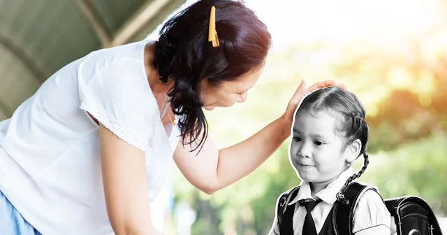 Mother stroking her daughter's hair while the daughter stands unamused as if she is unable to be sin...