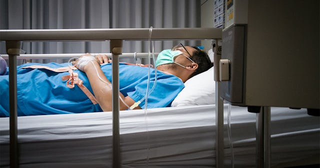 A middle-aged dad lying down in a hospital bed with a mask over his face who has Alzheimer's