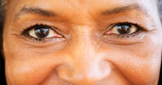A close-up of a woman's dark brown eyes with thin eyebrows and wrinkles on her forehead