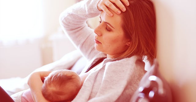A woman in a white hoodie breastfeeding her baby is in pain because of nipple thrush 