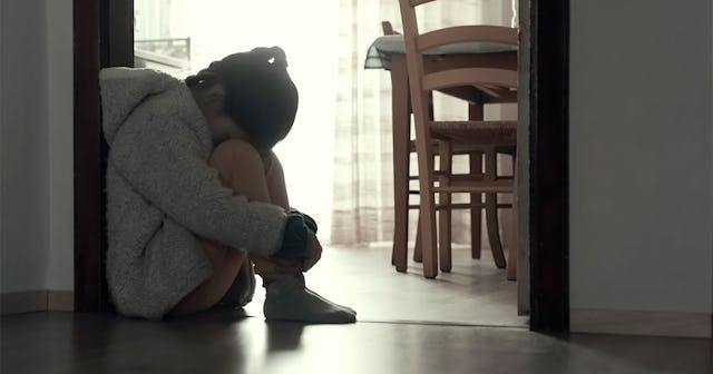 Depressed little girl sitting on the ground with her head on her knees while wearing a white jacket
