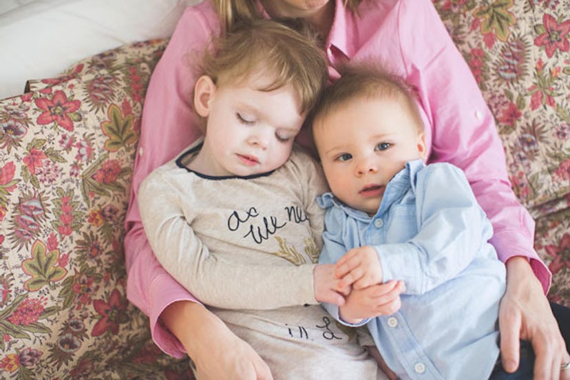 A mom wearing pink holding two toddlers in her arms