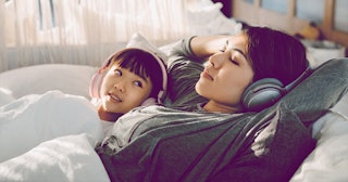 Kid laying with her mom in bed while listening to music.