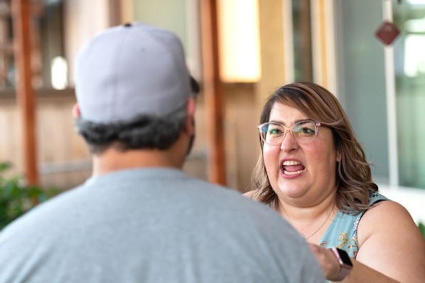 A woman in glasses yelling at a man in a baseball cap