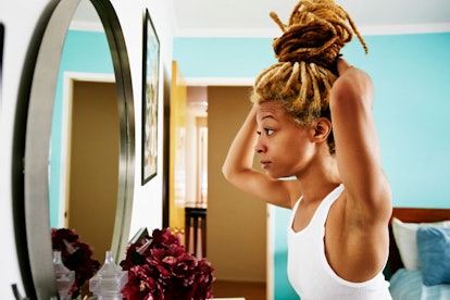 A woman looking at herself in the mirror and fixing her deadlocks