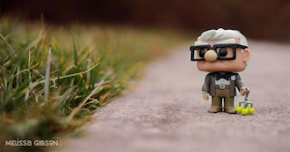 Grandpa from the cartoon "Up" as a little toy placed on a road surrounded by grass