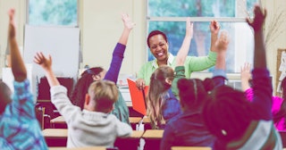 First grade class waving their hands with their teacher in a classroom