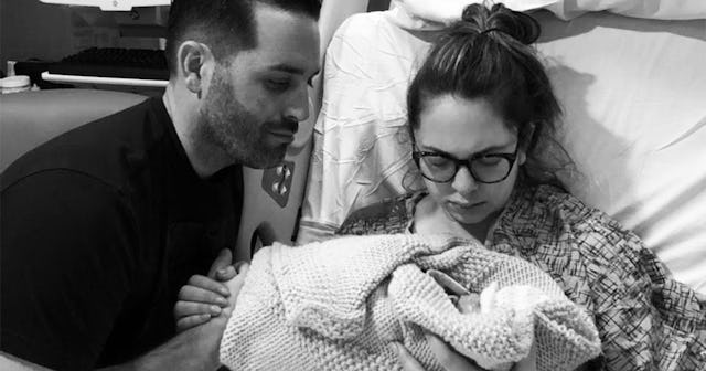 A young mother laying on the hospital bed while holding her stillborn child with her husband near he...