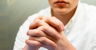 A woman in a white shirt with intertwined fingers in a praying position who is becoming the woman he...