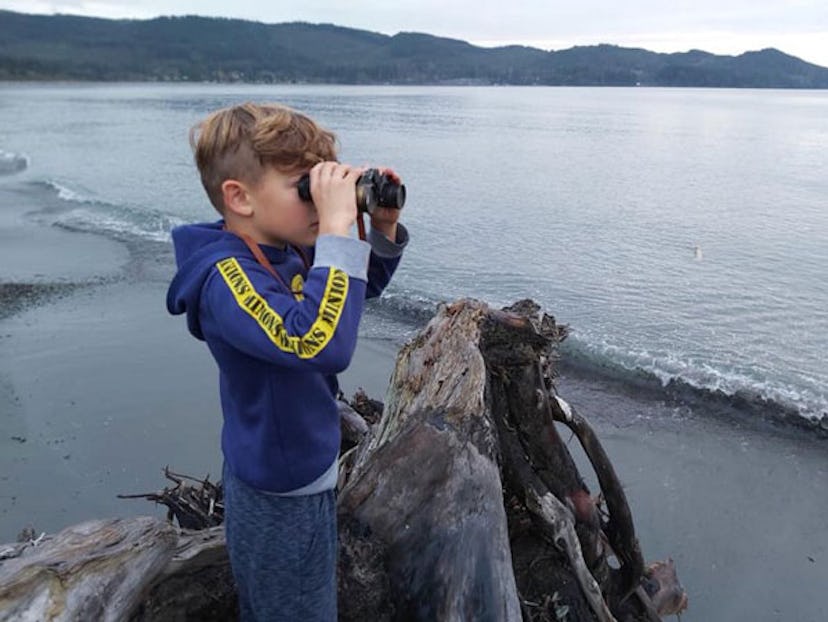 Christina Moog's older son watching through his binoculars while standing on a beach