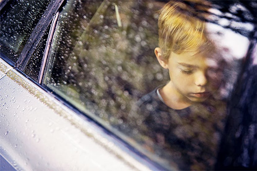 Depressed-looking blonde boy staring at the floor of a car while driving in it with the rain falling...