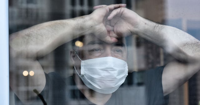 A sad man who has lost his restaurant to the pandemic wearing a mask and is leaning against a glass ...