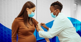 African American female doctor preparing a pregnant woman for vaccination. Pregnant woman getting a ...