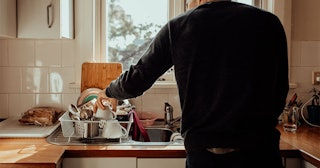 Rear view shot of an Australian man washing the dishes in front of a sunny kitchen window